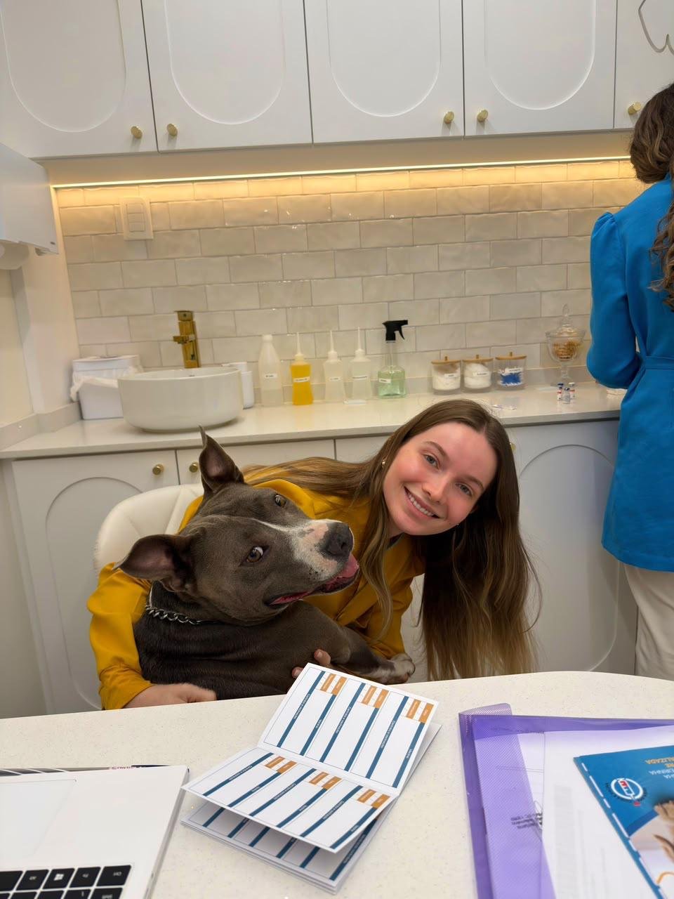 Dra. Diuly Correa Böger ao lado de um cão cinza em um consultório da Alluvie.